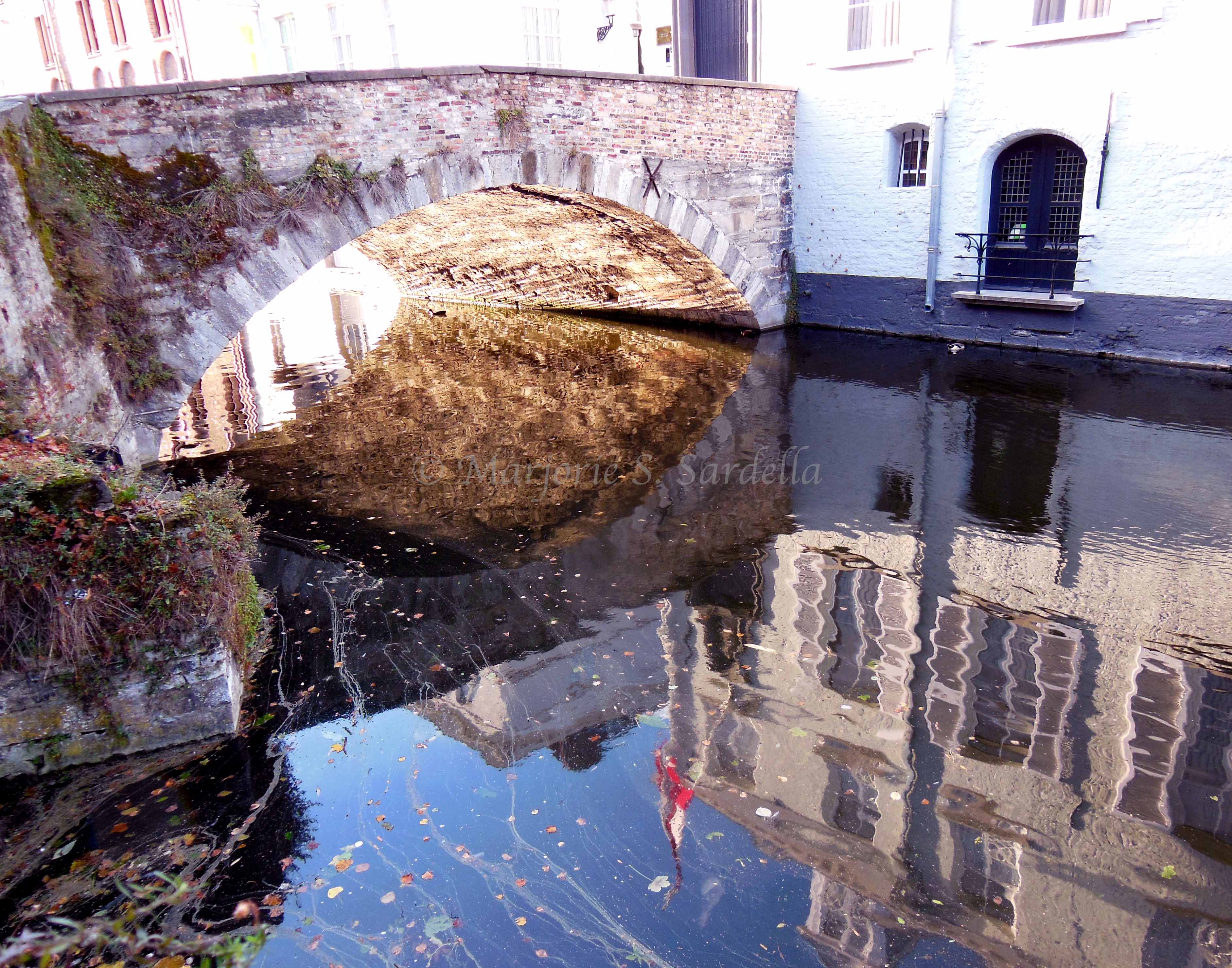 Arched Bridge Over a Canal in Bruges, Belgium, reflected in the water.